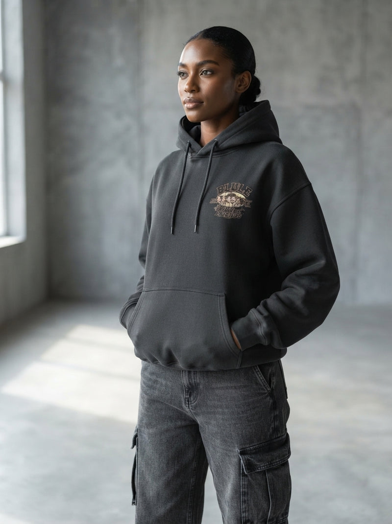 A fashion model wearing a charcoal hoodie in a minimalist, light-filled studio with a clean, out-of-focus background.
